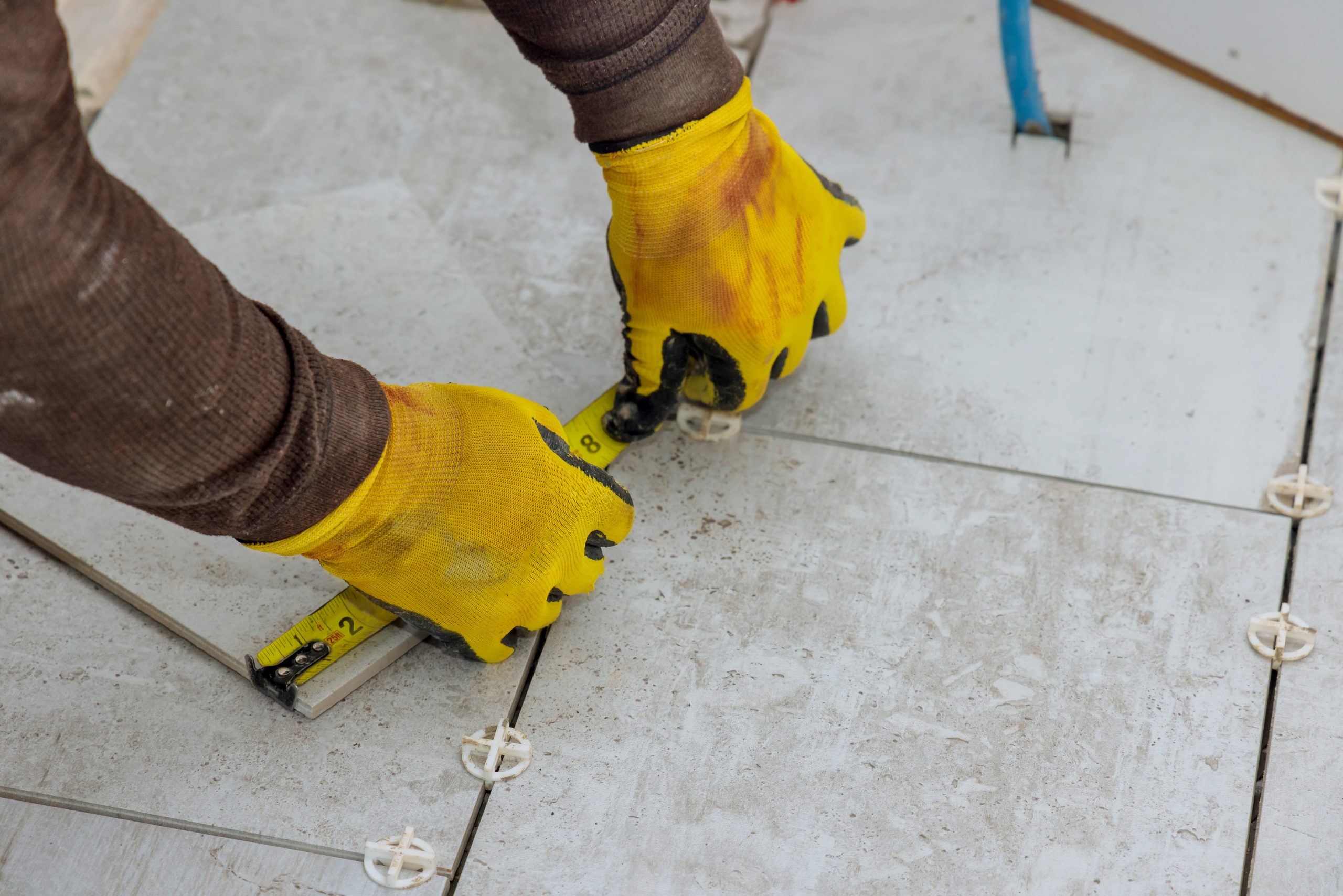 As contractor prepares to lay ceramic tiles on floor he measures tiles prior for cutting them