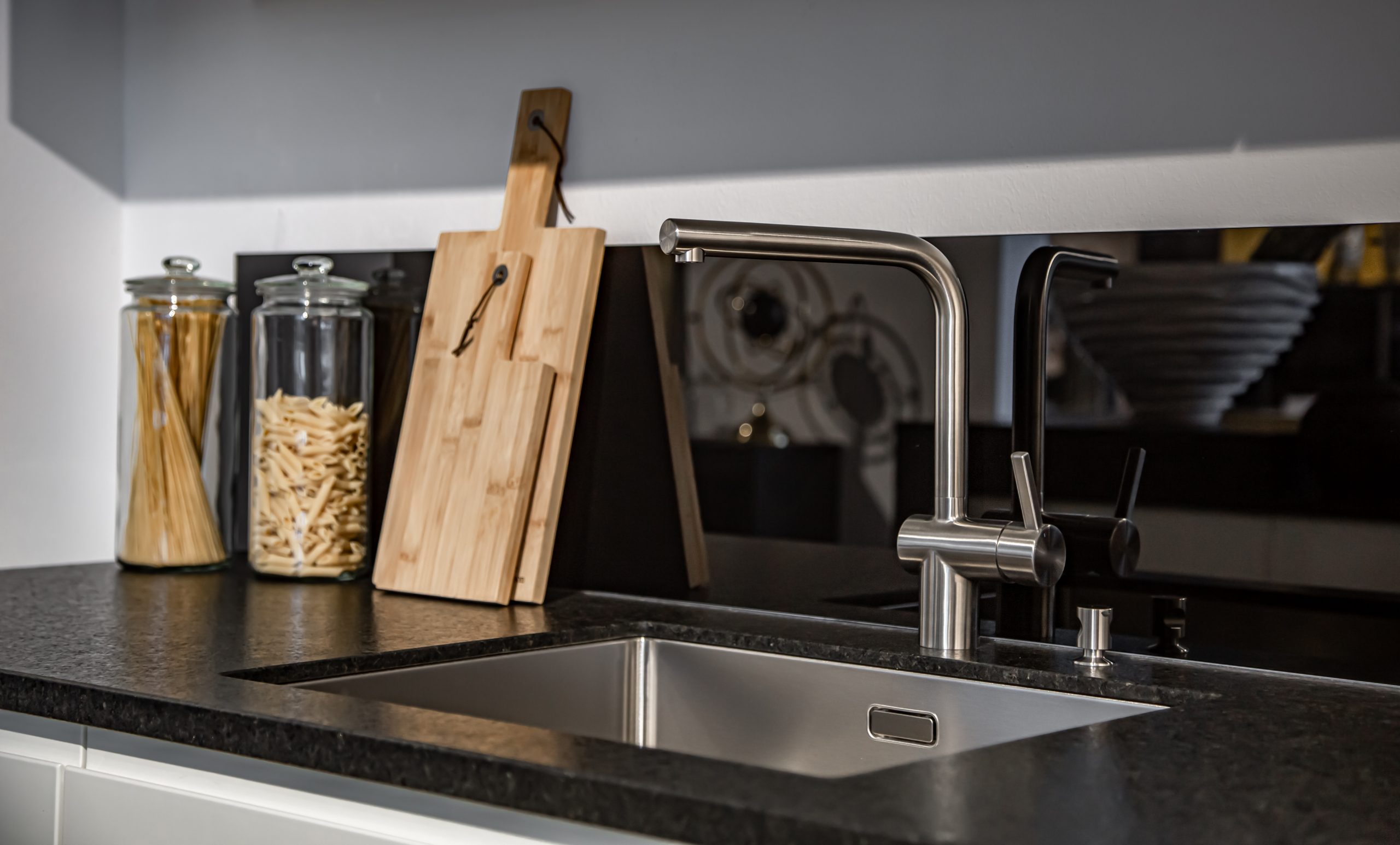 Modern designer chrome water tap over stainless steel kitchen sink close up.