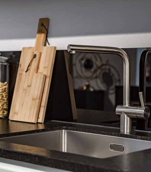 Modern designer chrome water tap over stainless steel kitchen sink close up.